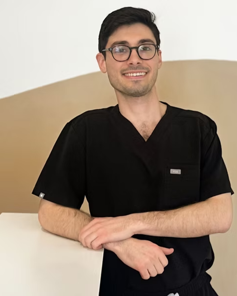 Portrait of Dr. Philip wearing black scrubs and glasses inside a modern dental clinic with warm, neutral design.